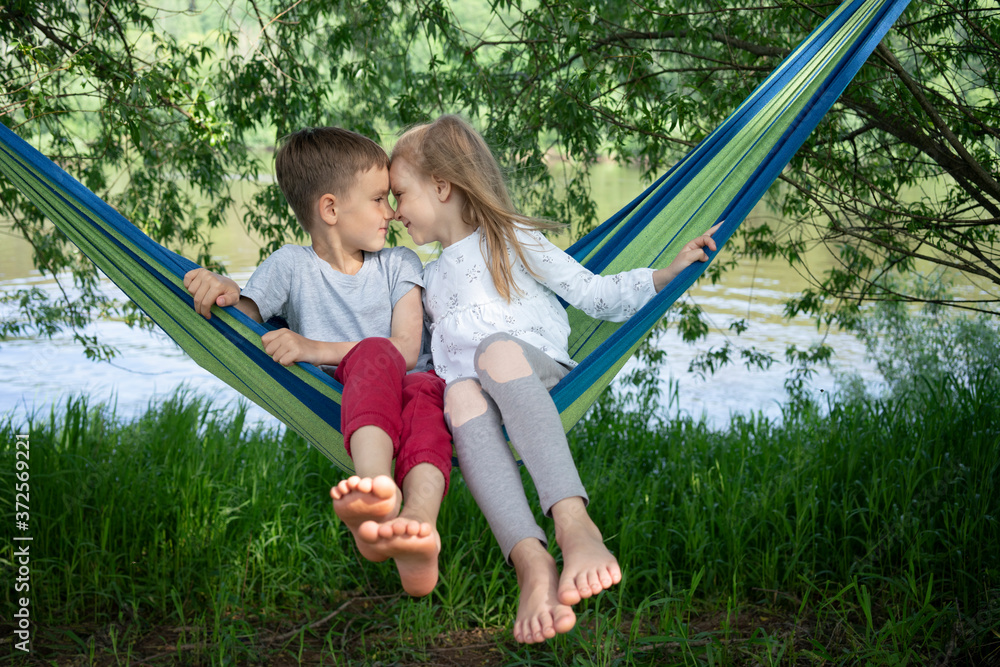 Cute friends with face to face sitting on hammock in forest Cute friends with face to face sitting on hammock in forest
