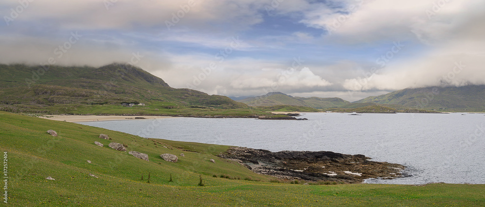 The lost Vally and Silver Strand beach of Uggool, county Mayo, Ireland. Nobody, Panorama image, green field, and beach, mountains in the background covered with low clouds.