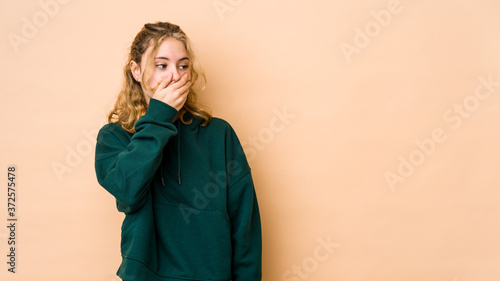 Young caucasian woman isolated on beige background thoughtful looking to a copy space covering mouth with hand. © Asier