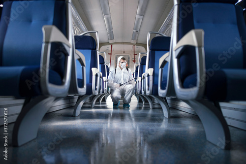 Public transportation healthcare. Man in white protection suit disinfecting and sanitizing subway train interior to stop spreading highly contagious coronavirus or COVID-19. photo