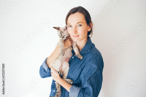 Fotografi Lifestyle photo of a cat sitter woman in casual clothes holding and hugging cute sleepy Devon Rex kitty