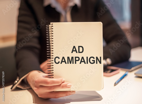 Closeup on business woman holding a notebook with text Ad Campaign, business concept image
