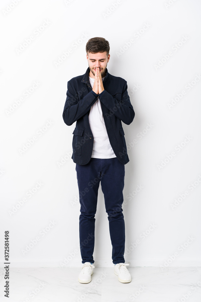 Full body young caucasian man isolated holding hands in pray near mouth, feels confident. Full body young caucasian man isolated holding hands in pray near mouth, feels confident.