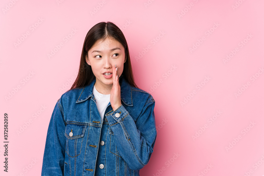 Fototapeta premium Young chinese woman posing in a pink background isolated is saying a secret hot braking news and looking aside
