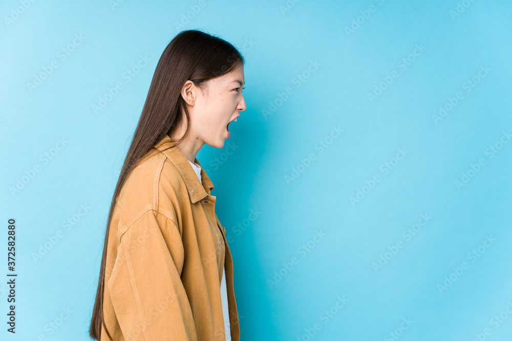 Young chinese woman posing in a blue background isolated shouting towards a copy space