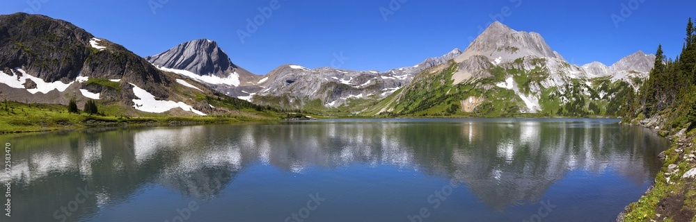 Wide Panoramic Landscape View of Scenic Aster Lake, Green Alpine Meadow and Rugged Rocky Mountain Peaks on a hiking trail in Kananaskis Country, Alberta, Canada on a sunny summertime day 