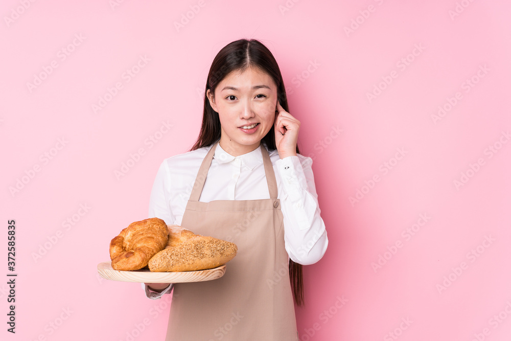 Young chinese baker woman isolated covering ears with hands. Young chinese baker woman isolated covering ears with hands.