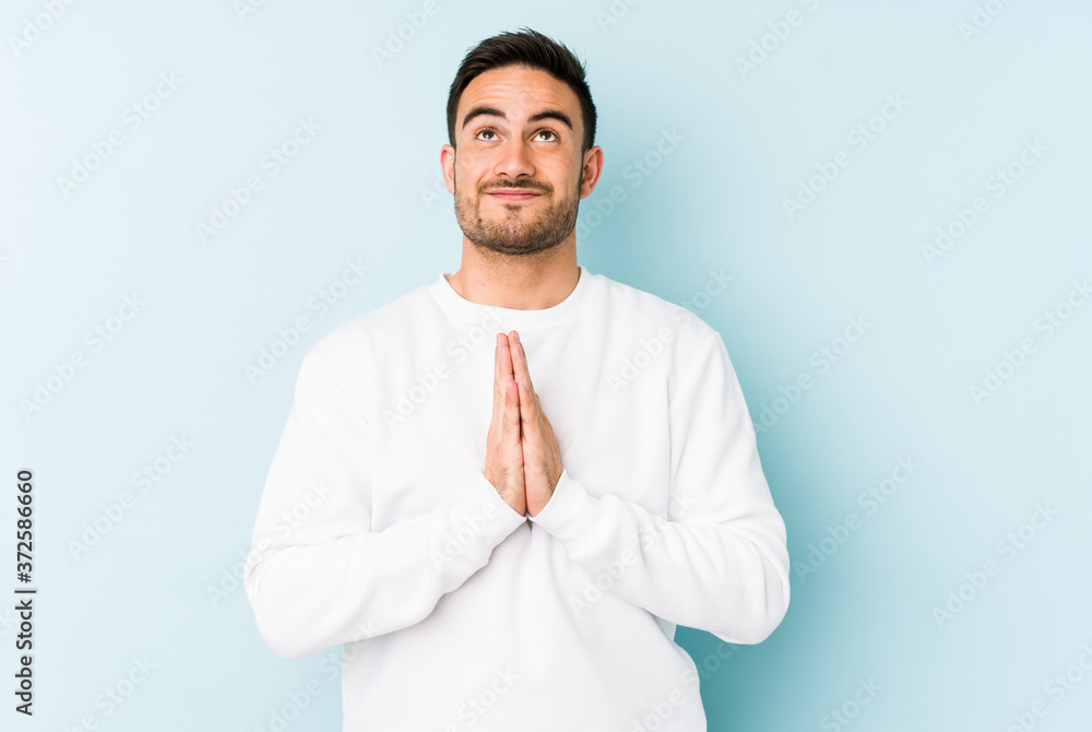Young caucasian man isolated on blue background holding hands in pray near mouth, feels confident. Young caucasian man isolated on blue background holding hands in pray near mouth, feels confident.