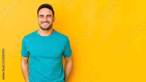 Young caucasian man isolated on yellow bakground laughs and closes eyes, feels relaxed and happy.