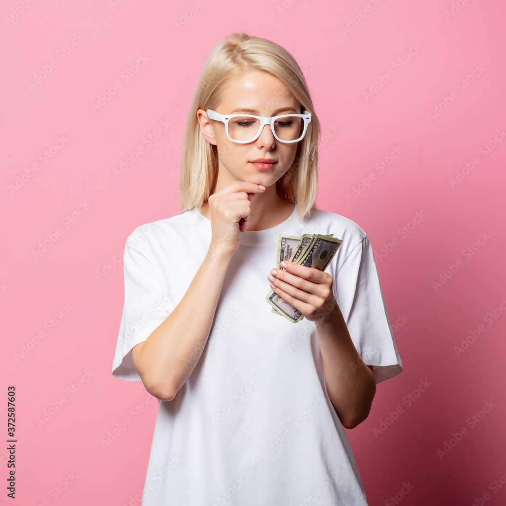 Blonde woman in white moch-up tshirt and glasses with money on pink background Blonde woman in white moch-up tshirt and glasses with money on pink background