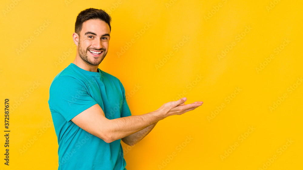 Young caucasian man isolated on yellow bakground holding a copy space on a palm. Young caucasian man isolated on yellow bakground holding a copy space on a palm.