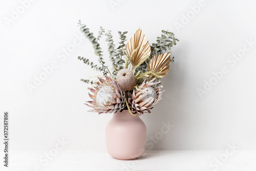 Fototapeta Naklejka Na Ścianę i Meble -  Beautiful dried flower arrangement in a stylish pink vase. In the flower bunch is pink King Proteas, Banksia, Eucalyptus leaves and golden Palm fronds, photographed on a white background.