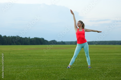 young woman doing yoga exercises on a large meadow of lawn grass
