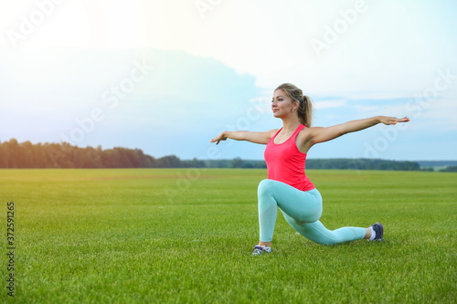 young woman doing yoga exercises on a large meadow of lawn grass