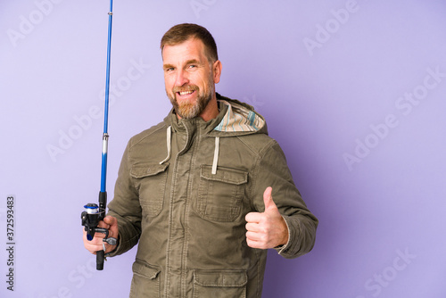 Senior fisherman isolated on purple background smiling and raising thumb up