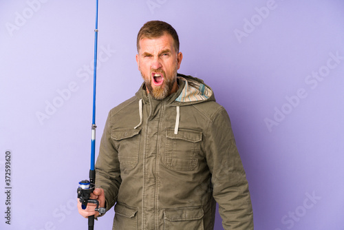Senior fisherman isolated on purple background screaming very angry and aggressive.