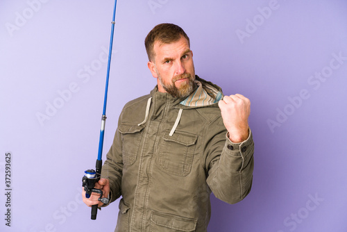 Senior fisherman isolated on purple background showing fist to camera, aggressive facial expression.