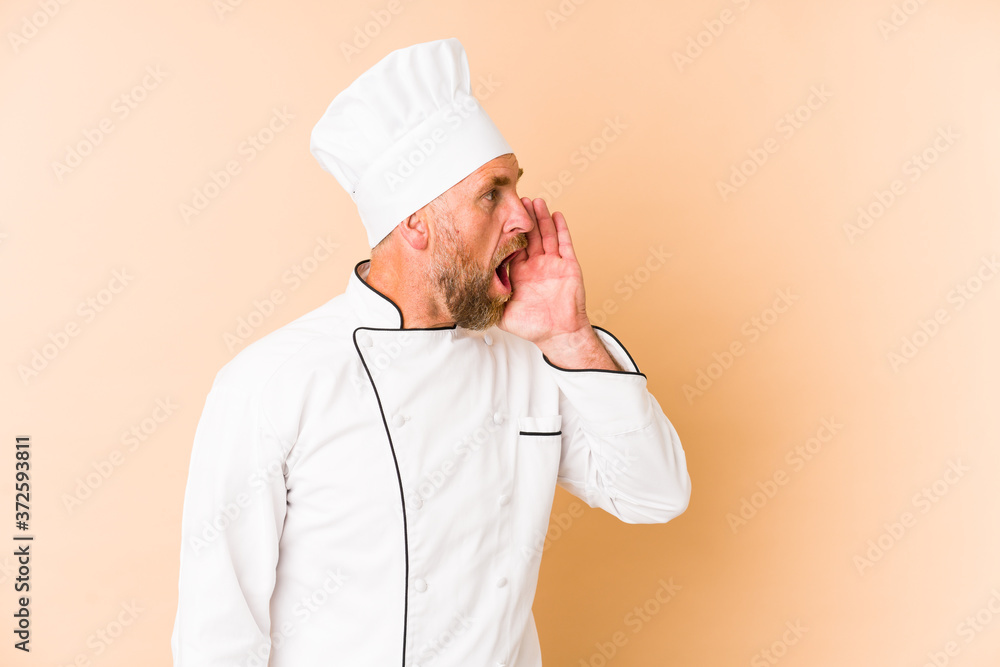 Chef man isolated on beige background shouting and holding palm near opened mouth. Chef man isolated on beige background shouting and holding palm near opened mouth.