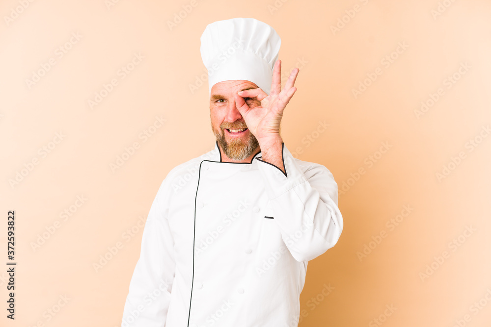 Chef man isolated on beige background excited keeping ok gesture on eye. Chef man isolated on beige background excited keeping ok gesture on eye.