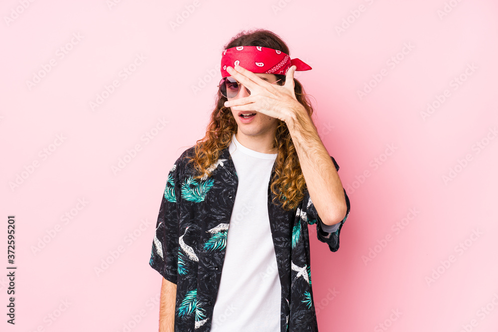 Young hippie caucasian man isolated blink at the camera through fingers, embarrassed covering face. Young hippie caucasian man isolated blink at the camera through fingers, embarrassed covering face.