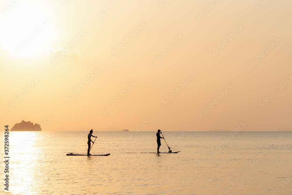 Couple swims on paddle boards on the sea against the backdrop of islands and golden sunset