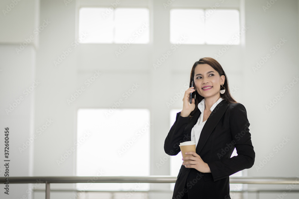Portrait of a young Asian business woman talking over cellphone and holding cup of coffee in business building. Photo of beautiful girl in casual suite with phone and cup of coffee. Portrait of a young Asian business woman talking over cellphone and holding cup of coffee in business building. Photo of beautiful girl in casual suite with phone and cup of coffee.