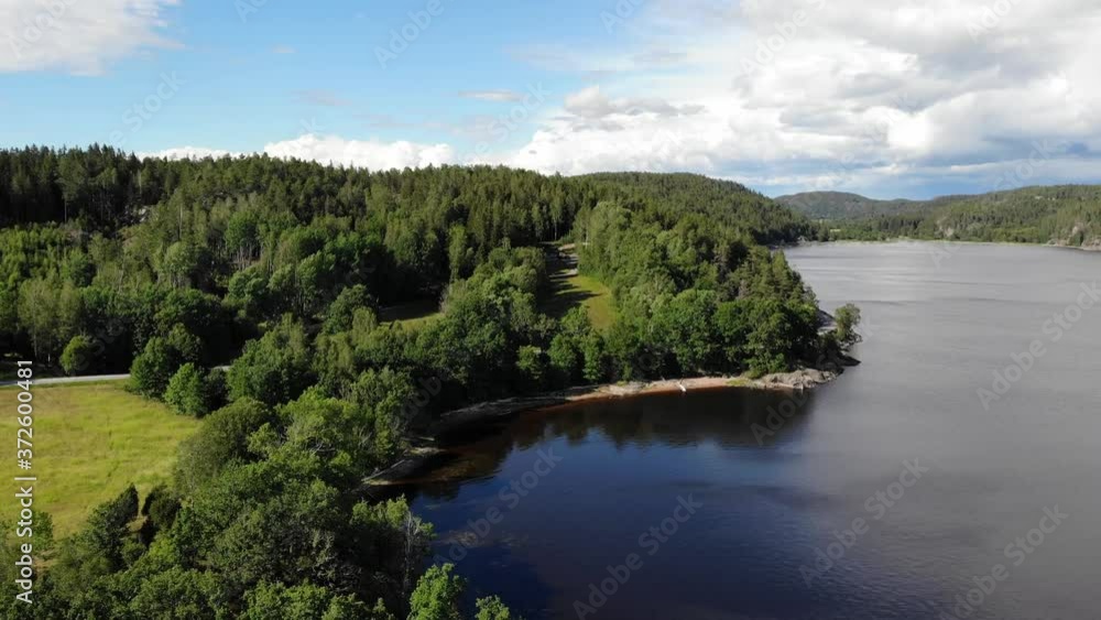 Drone descend near beautiful lake shore with green meadow, light blue water and green trees Drone descend near beautiful lake shore with green meadow, light blue water and green trees