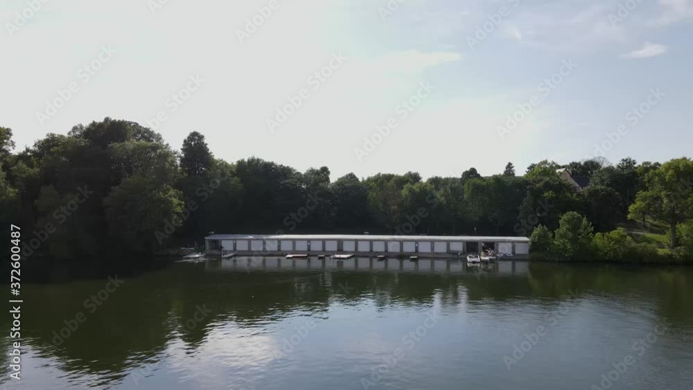 Aerial view of boat shed with boat storing units and motorboats on a calm still lake. Flying along an isolated boat storage unit with boats waiting to be docked inside. Aerial view of boat shed with boat storing units and motorboats on a calm still lake. Flying along an isolated boat storage unit with boats waiting to be docked inside.
