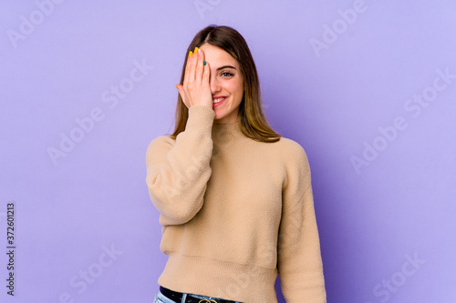 Young caucasian woman isolated on purple background having fun covering half of face with palm.