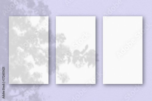 3 vertical sheets of textured white paper on lilac table background. Mockup overlay with the plant shadows. Natural light casts shadows from an exotic plant. Horizontal orientation