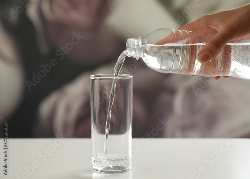Woman pouring water from bottle into glass on table against blurred background, closeup
