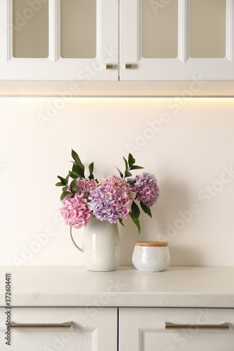 Bouquet with beautiful purple hydrangea flowers and jar on light countertop