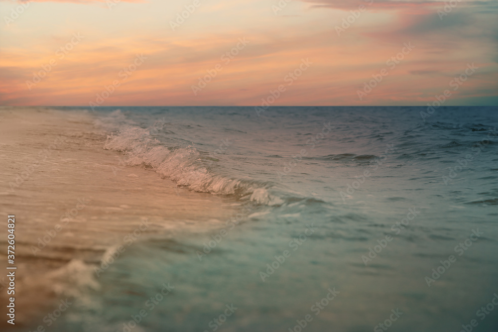 Ocean waves rolling on sandy beach under sky with clouds at sunset, closeup