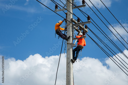 An electrician is on a light pole to maintain a high voltage line on a dangerous electric pole.