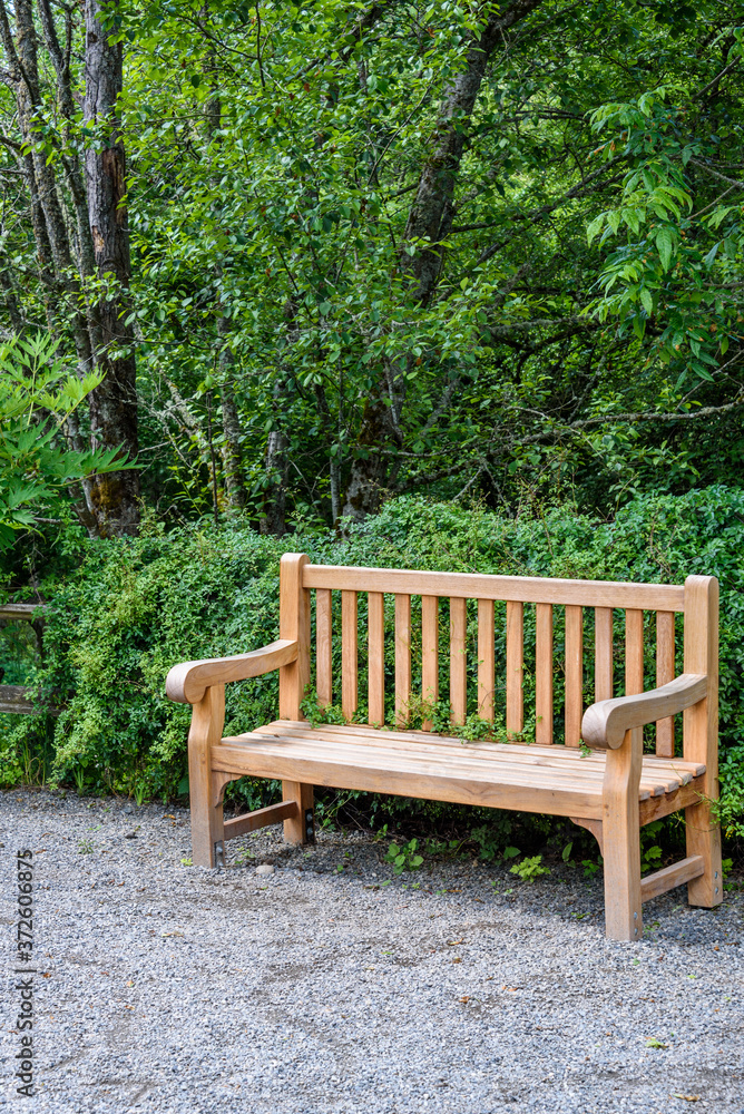 Wooden bench in off a gravel path in a park, ready for a rest stop
