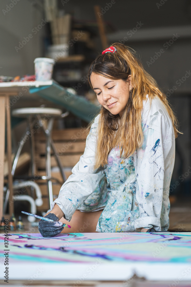 Cheerful barefoot female artist in dirty robe and gloves lying on wooden floor with closed eyes in front of abstract painting in art studio Cheerful barefoot female artist in dirty robe and gloves lying on wooden floor with closed eyes in front of abstract painting in art studio