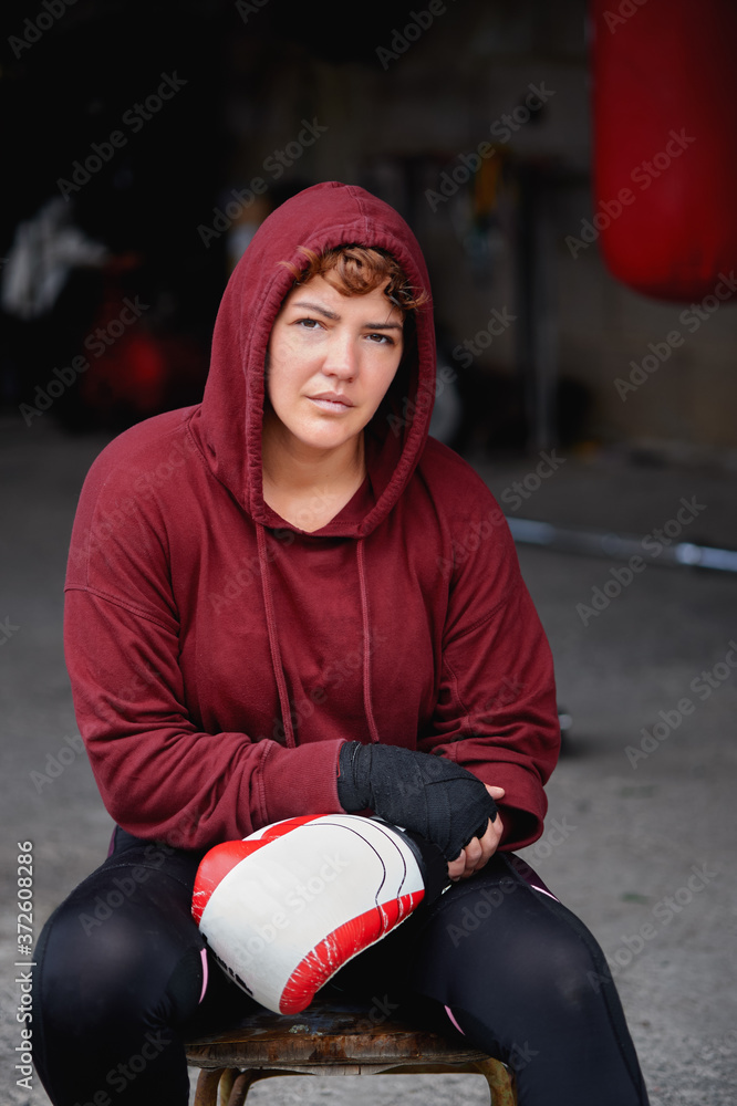 Concentrated female boxer in leggings and hoodie wrapping hands with
