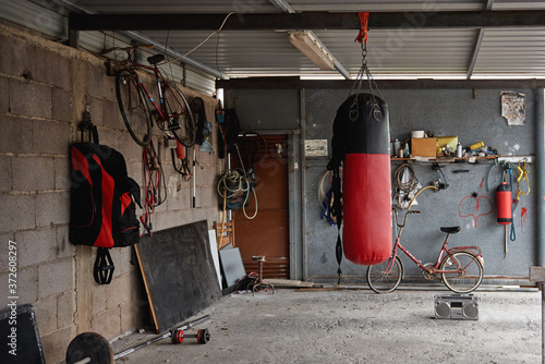 Interior of shabby country garage gym with boxing bag bicycles and sports equipment placed on concrete floor near old fashioned boombox photo