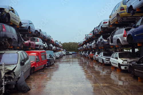 Rubbish dump with pile of multicolored modern automobiles after accident with dents on surface on wet road under blue sky in town photo