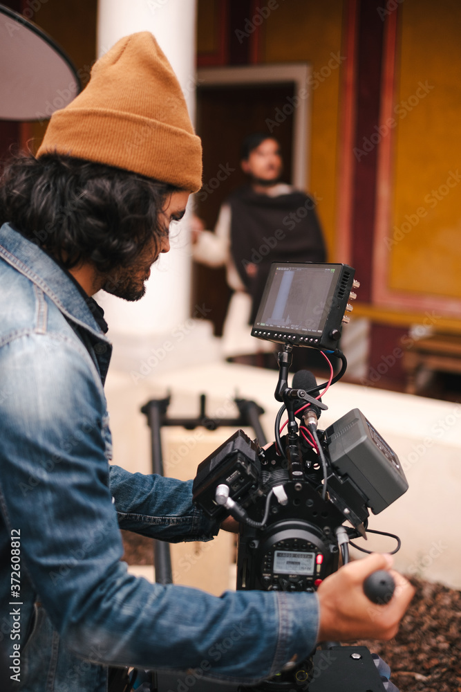 Side view faceless male video operator in casual denim jacket and hat shooting video of actor on modern professional camera Side view faceless male video operator in casual denim jacket and hat shooting video of actor on modern professional camera