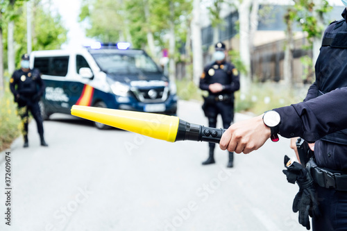 Crop anonymous police officer prohibiting car driving on street with yellow traffic baton during coronavirus on sunny day photo