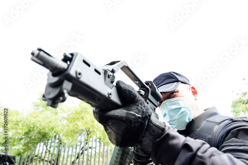 From below of serious spec ops police officer in  protective uniform and medical mask aiming submachine gun during police operation photo