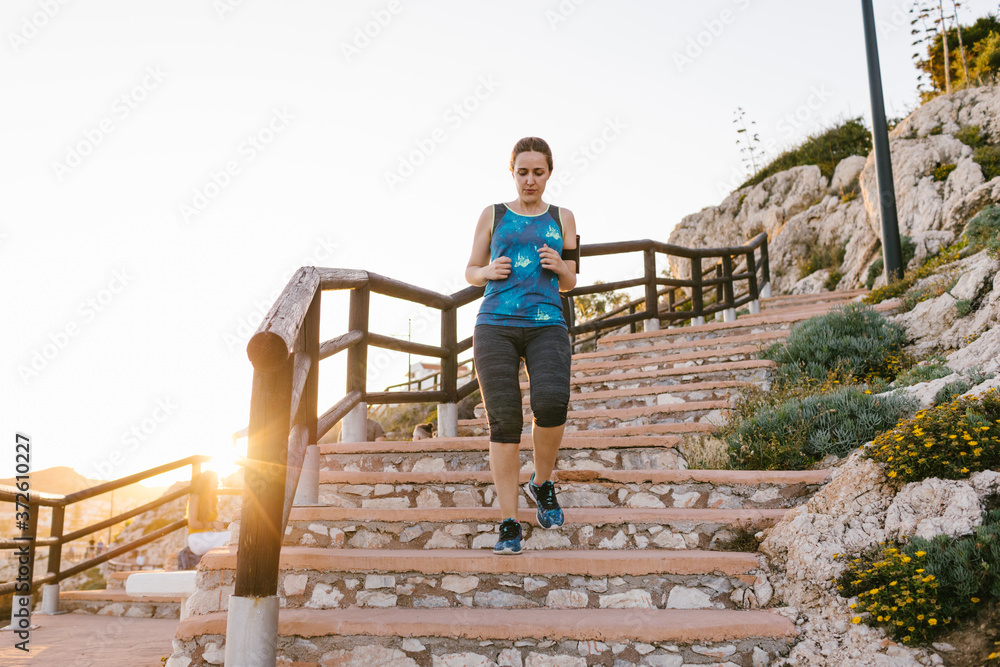 Low angle of sportswoman in t shirt and leggings running down stone steps while training during sunset Low angle of sportswoman in t shirt and leggings running down stone steps while training during sunset