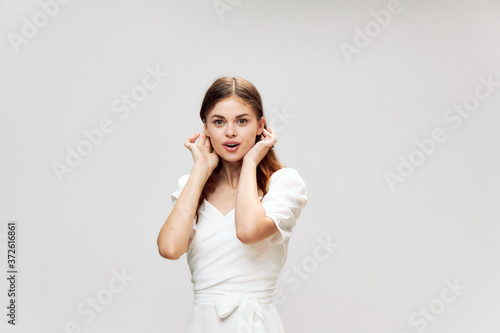 Woman straightens her hair white dress smile look ahead gray background 