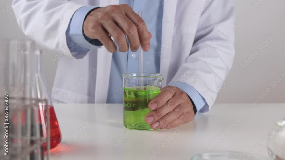 Young Scientist Man in Lab Coat Stir Green Solution in Beaker for Testing. Scientist Man Working in Laboratory in Corona Virus Disease or Covid 19 Situation Young Scientist Man in Lab Coat Stir Green Solution in Beaker for Testing. Scientist Man Working in Laboratory in Corona Virus Disease or Covid 19 Situation