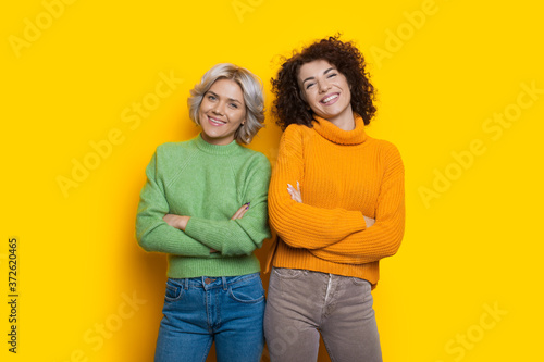 Caucasian women with curly hair are posing on a yellow studio wall with crossed hands © Strelciuc