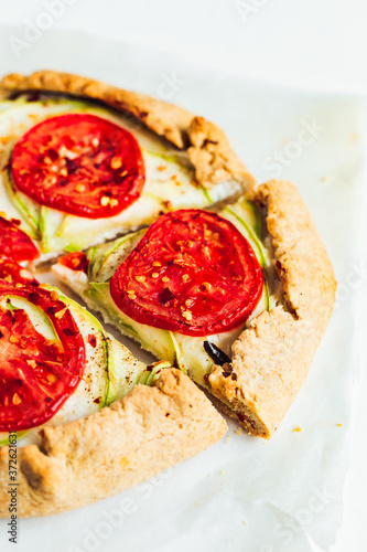 A close-up of a galette with ricotta cheese, zucchini and tomatos, white baking paper, white background