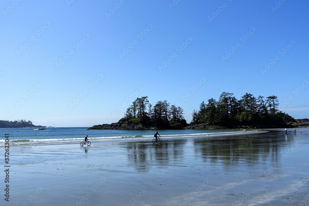 People biking along the hard sand at low tide with the ocean in the background at Chesterman Beach outside Tofino, British Columbia, Canada.