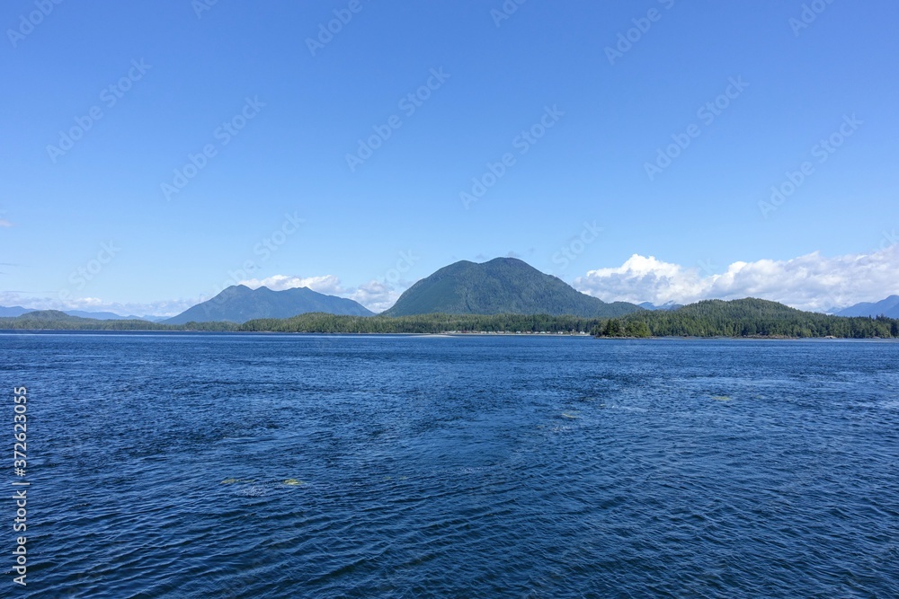 A beautiful vast full view blue seascape ocean photo with forested mountains in the background on a beautiful summer day in a tofino A beautiful vast full view blue seascape ocean photo with forested mountains in the background on a beautiful summer day in a tofino