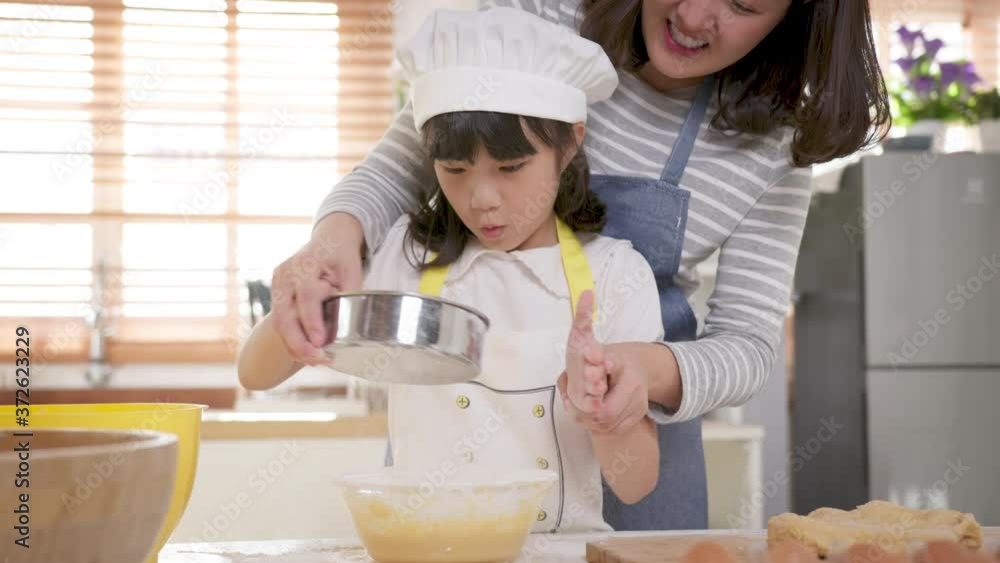 Close up Happy asian mother helping little kid daughter child preparing bakery in kitchen at home. Happy adorable little child girl in apron enjoying cooking homemade meal together with mommy at home. Close up Happy asian mother helping little kid daughter child preparing bakery in kitchen at home. Happy adorable little child girl in apron enjoying cooking homemade meal together with mommy at home.